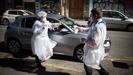 Deux infirmiers d'un laboratoire d'analyse dans le 10e arrondissement de Paris, réalisent un test de dépistage PCR au coronavirus en "drive in", le 30 mars 2020. (BENJAMIN MENGELLE / HANS LUCAS / AFP)