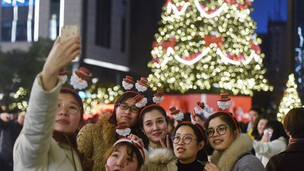 Des jeunes femmes se prennent devant un sapin de Noël en Chine, le 24 décembre 2018, à Hangzhou. (STR / AFP)