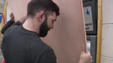 Un menuisier protège la facade d'une banque à Bourges (Cher) le 11 janvier (Capture d'écran France 2)