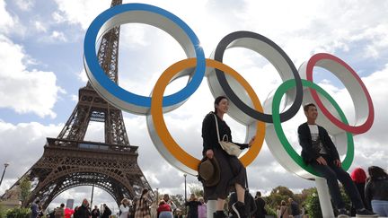 Des touristes posent devant les anneaux olympiques désormais installés au pied de la tour Eiffel, le 27 septembre 2024. (THOMAS SAMSON / AFP)