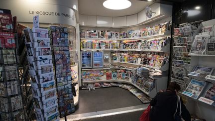 Une femme cherche un magazine dans un kiosque à journaux de Paris, en mars 2020, au début de la pandémie de Covid-19. (JOEL SAGET / AFP)