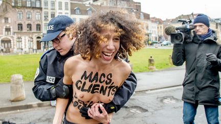 Un policier arr&ecirc;te une Femen qui vient de se jeter sur la voiture de DSK, peu avant l'audience du 10 f&eacute;vrier 2015 dans le proc&egrave;s du Carlton, &agrave; Lille (Nord).&nbsp; (PHILIPPE HUGUEN / AFP)