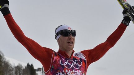 Dario Cologna lève les bras à l'arrivée du skiathlon (ODD ANDERSEN / AFP)