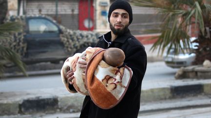 Un homme évacue un enfant d'Alep-Est (Syrie), le 12 décembre 2016.&nbsp; (ABDALRHMAN ISMAIL / REUTERS)