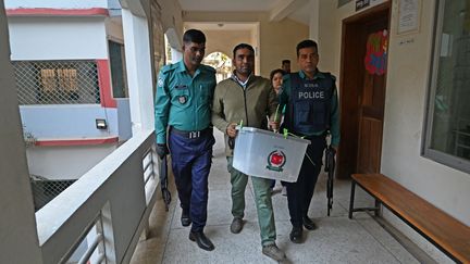 Escorté par deux policiers, un assesseur d'un bureau de vote transporte une urne électorale pleine de bulletins, le 7 janvier 2024 à Decca (Bangladesh). (MUNIR UZ ZAMAN / AFP)