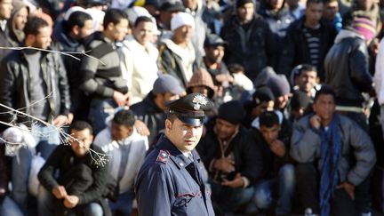 Un policier italien devant des migrants arrivés de Tunisie sur l'île de Lampedusa le 13 février 2011. (REUTERS/Antonio Parrinello)