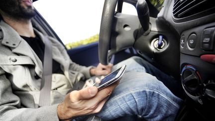 Un homme regarde son portable en conduisant. (CAMILLE MAZOYER / MAXPPP)