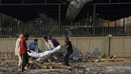 Des bénévoles préparent le corps d'un homme mort du Covid-19 avant le rituel de la crémation, le 12 mai 2021 à New Delhi. (ARUN SANKAR / AFP)