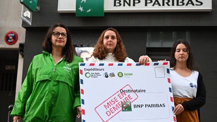 Trois militantes écologistes devant une agence de la BNP Paribas à Paris, le 26 octobre 2022. &nbsp; (EMMANUEL DUNAND / AFP)