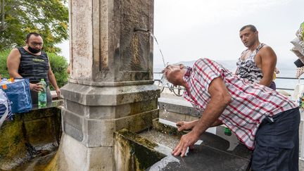 Des hommes se rafraîchissent à une fontaine, mercredi 11 août 2021 à Messine (Italie). (GIOVANNI ISOLINO / AFP)