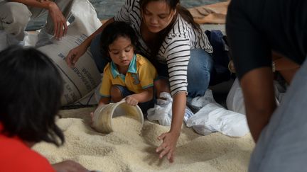 Une m&egrave;re et son fils apportent leur aide, &agrave; Manille, en remplissant des sacs de riz, destin&eacute;s aux survivants du typhon. (JAY DIRECTO / AFP)