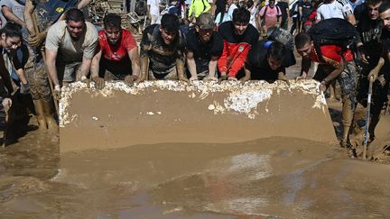 Des habitants utilisent des plaques pour évacuer la boue après les inondations, à Paiporta. (JOSE JORDAN / AFP)