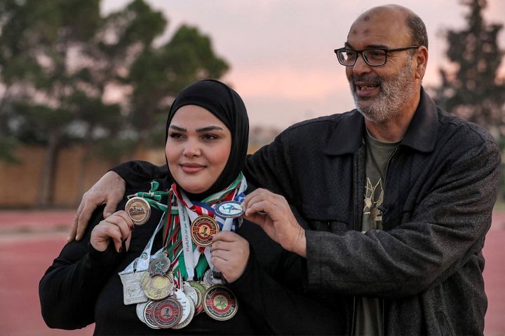 Retaj al-Sayeh pose aux côtés de son père et entraîneur, Salem al-Sayeh, et avec ses nombreuses médailles autour du cou.  (MAHMUD TURKIA / AFP)