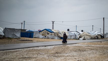 Une femme passe devant des tentes sous la pluie au Camp Roj (Syrie), où sont détenus des proches de personnes soupçonnées d'appartenir au groupe État islamique, le 4 mars 2021. (DELIL SOULEIMAN / AFP)