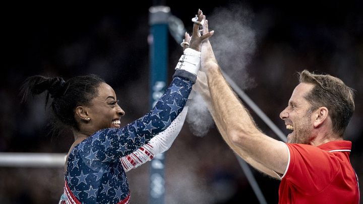 Simone Biles et Laurent Landi lors de l'épreuve des barres asymétriques du concours général par équipes, aux JO de Paris, le 30 juillet 2024, à l'Arena de Bercy. (AYTAC UNAL / AFP)