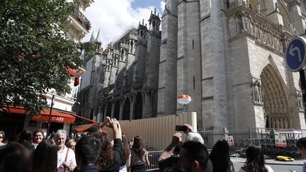 Des touristes viennent photographier la cathédrale Notre-Dame de Paris après l'incendie, le 15 juin 2019. (ZAKARIA ABDELKAFI / AFP)