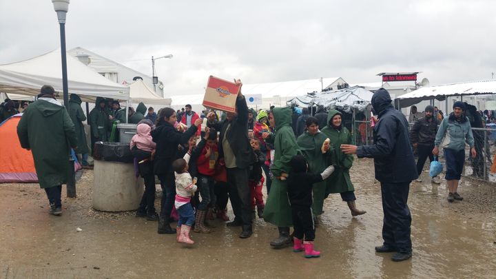 Des enfants s'agitent autour d'un homme qui distribue des petites trompettes en plastique, dans le camp de migrants d'Idomeni (Grèce), le 16 mars 2016.&nbsp; (LOUIS SAN / FRANCETV INFO)