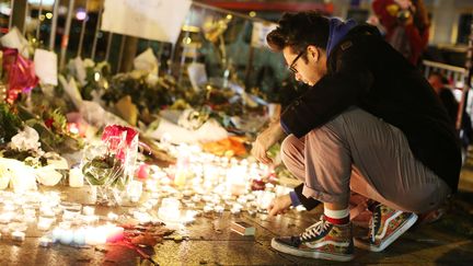 Un homme&nbsp;allumant une bougie devant le Bataclan, le 14 novembre 2015, au lendemain de l'attaque terroriste.&nbsp; (MALTE CHRISTIANS / DPA / AFP)