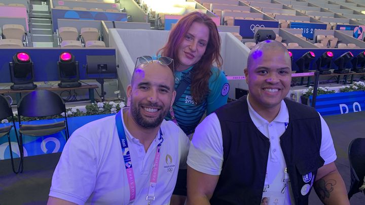 Nacer Zorgani avec Eva, l'une des bénévoles qui l'aide, et Michael Markham, le présentateur anglophone de boxe aux JO, le 9 août 2024 à Roland-Garros. (GABRIEL JOLY)