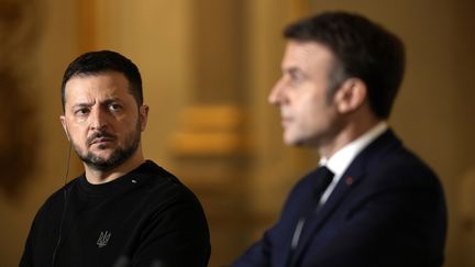 La président ukrainien Volodymyr Zelensky (à gauche) regarde Emmanuel Macron lors d'une conférence de presse à l'Élysée, le 16 février 2024, (THIBAULT CAMUS / POOL / AFP)