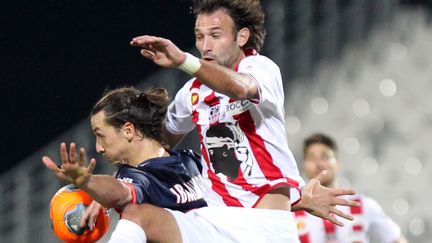 L'attaquant du PSG Zlatan Ibrahimovic charg&eacute; par le d&eacute;fenseur ajaccien C&eacute;dric Hengbart, lors du match Ajaccio-PSG, le 11 janvier 2014, &agrave; Ajaccio.&nbsp; (PASCAL POCHARD-CASABIANCA / AFP)