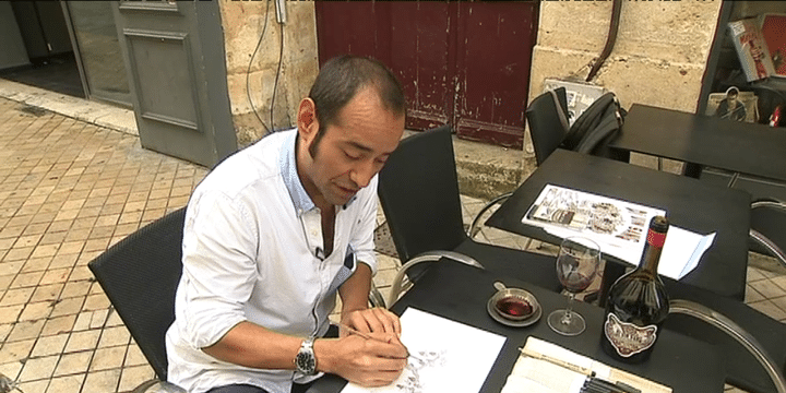 Mauro Ceballos en train de peindre. A côté de lui une soucoupe pleine de vin rouge, le pigment qu'il a choisi.
 (France 3 / Culturebox)