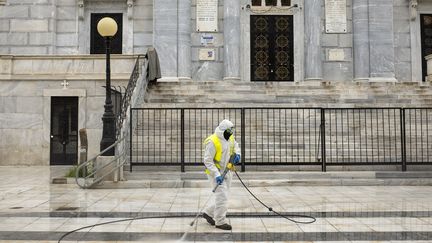 Un employé municipal désinfecte une rue d'Athènes devant une église, le 7 avril 2020 (ANGELOS TZORTZINIS / AFP)