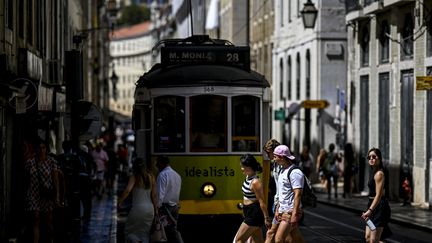 Des touristes traversent une rue devant un tramway au centre-ville de Lisbonne, au Portugal, le 16 août 2023. (PATRICIA DE MELO MOREIRA / AFP)