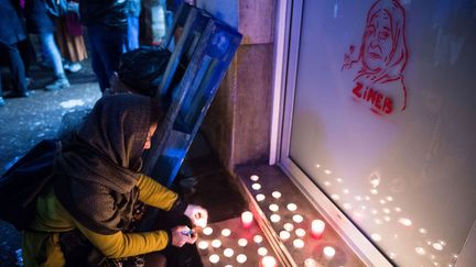 Une femme allume des bougies devant un portrait de Zineb Redouane alors que les gens se rassemblent le 1er décembre 2019 à Marseille pour rendre hommage à la vieille dame. (CLEMENT MAHOUDEAU / AFP)