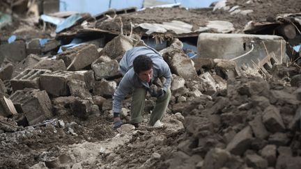 Un homme regarde sous les d&eacute;combres d'un immeuble, le 29 octobre 2011,&nbsp;dans le village de Guvecli, touch&eacute; par le s&eacute;isme en Turquie. (MORTEZ NIKOUBAZL / REUTERS)