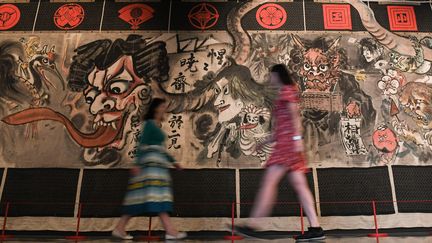 Des employées du British Museum passent devant un rideau historique de théâtre Manga peint par l'artiste japonais&nbsp;Kawanabe Kyosai&nbsp;pour le théâtre Shintomi, à Londres, le 22 mai 2019. (DANIEL LEAL-OLIVAS / AFP)