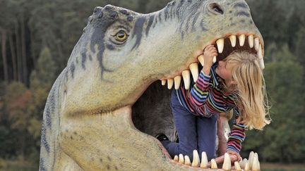 Une petite fille joue dans la gueule d'une r&eacute;plique de dinosaure expos&eacute;e au "Monde des dinosaures" &agrave; Hohenfelden (Allemagne), le 25 septembre 2012. (JENS MEYER / AP / SIPA)