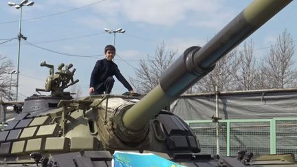 Un enfant pose sur un tank, à l'exposition sur les forces armées iraniennes, à Téhéran, le 10 février 2019. (GILLES GALLINARO / RADIO FRANCE)