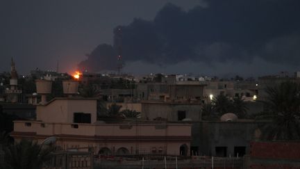 Des flammes et la fum&eacute;e se d&eacute;gagent, le 29 juillet au matin, de l'incendie d'une citerne de carburant &agrave; Tripoli, caus&eacute; la veille par des combats entre deux milices rivales pour le contr&ocirc;le de l'a&eacute;roport voisin. Mardi soir, le feu n'&eacute;tait toujours pas maitris&eacute;. (SABRI ELMHEDWI / MAXPPP)