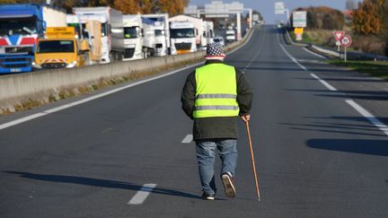 Un homme vêtu d'un gilet jaune marche sur une route nationale bloquée par le mouvement, près du dépôt de pétrole de la Rochelle (Charente-Maritime), le 19 novembre 2018.&nbsp; (XAVIER LEOTY / AFP)