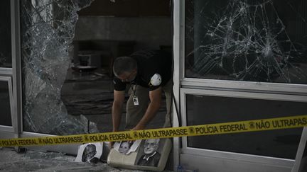 Un policier ramasse des portraits déchirés dans le bâtiment de la Cour suprême à Brasilia, le 10 janvier 2023, deux jours après que des milliers de partisans de l'ex-président d'extrême droite brésilien Jair Bolsonaro ont fait irruption dans des bâtiments fédéraux. (CARL DE SOUZA / AFP)