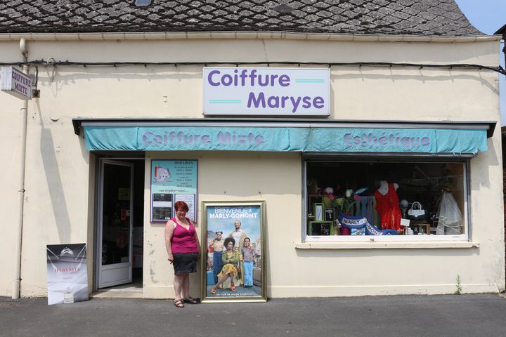 Maryse Delache devant son salon de coiffure à côté de l'affiche du film "Bienvenue à Marly-Gomont", le 8 juin 2016 à Marly-Gomont (Aisne). (BENOIT ZAGDOUN / FRANCETV INFO)