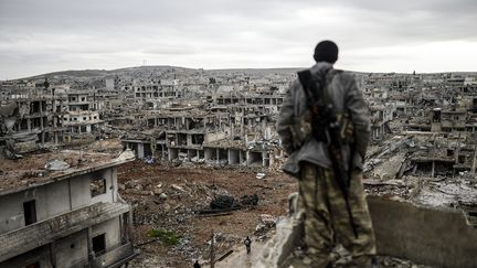 Un combattant kurde devant la ville de Kobane (Syrie) ravagé par la guerre, en janvier 2015. (BULENT KILIC / AFP)