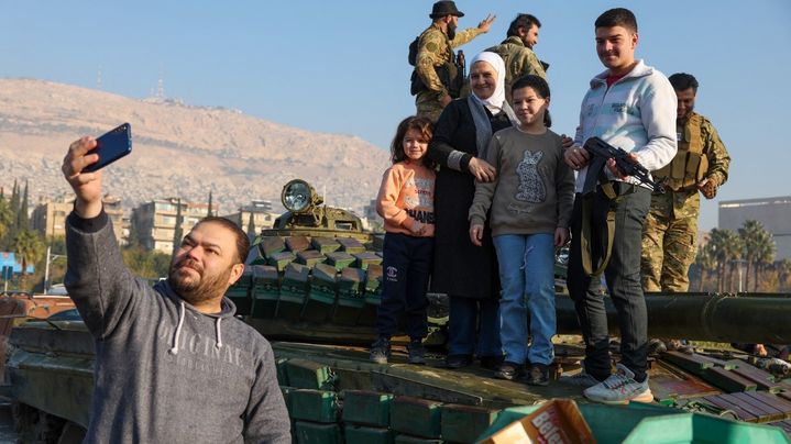 Un homme se prend en photo, avec sa famille, devant un char à Damas, en Syrie, après la chute du régime Assad, lundi 9 décembre 2024. (OMAR HAJ KADOUR / AFP)