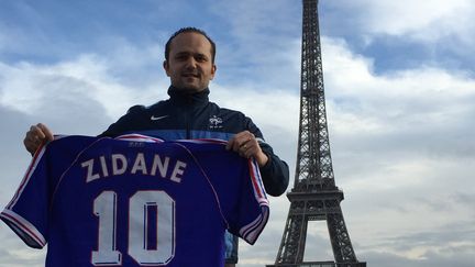 Le collectionneur Olivier Démolis pose avec son maillot de Zinédine Zidane, porté pendant la finale de la Coupe du monde 1998, devant la Tour Eiffel, à Paris. (OLIVIER DEMOLIS / DR)