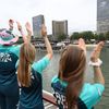 Des volontaires sur le bateau de la délégation française encouragent un autre bateau naviguant devant la Bibliothèque nationale de France sur la Seine, lors de la cérémonie d'ouverture des Jeux olympiques de Paris, le 26 juillet 2024. (FRANCK FIFE / AFP)