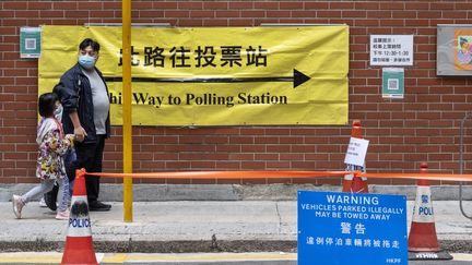 Un homme et sa fille entrent dans un bureau de vote, le 19 décembre 2021 à Hong Kong (Chine). (MIGUEL CANDELA / ANADOLU AGENCY / AFP)