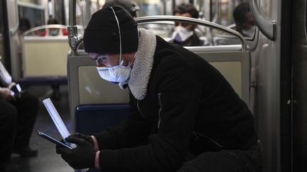 Un jeune homme masqué regarde son smartphone. (ALAIN JOCARD / AFP)