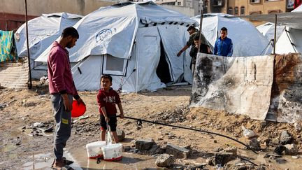 Un enfant remplit des seaux d'eau près de tentes de Palestiniens déplacés à Gaza, dans la bande de Gaza, le 11 décembre 2024. (OMAR AL-QATTAA / AFP)