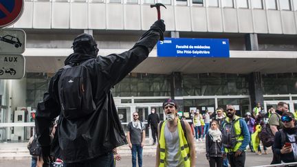 Un membre des "Black Block" brandit un marteau devant un bâtiment de la faculte de médecine de la Pitié Salpétrière lors de heurts avec la police en marge de la manifestation unitaire du 1er mai 2019 à Paris. (CHRISTOPHE PETIT TESSON / MAXPPP)