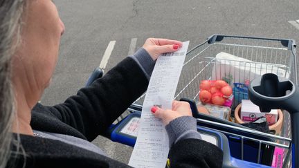 Une femme vérifie son ticket de caisse au dessus d'un chariot plein d'aliments. (RICHARD VILLALON / MAXPPP)