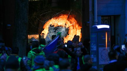 Des manifestants devant une vitrine brisée lors de "l'acte III" de la mobilisation des "gilets jaunes", le 1er décembre 2018 à Paris. (GEOFFROY VAN DER HASSELT / AFP)