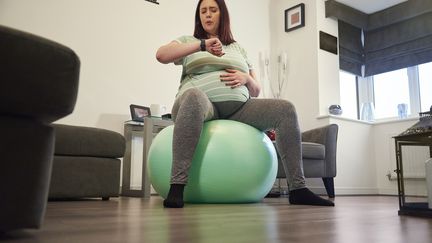 A pregnant woman, sitting on an exercise ball, calculates the rate of her contractions on her watch.  (Illustration) (MARTINPRESCOTT / E+ / GETTY IMAGES)