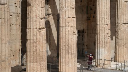 Une employée du ministère de la Culture grec nettoie une vitre en plexiglas sur l'acropole, à Athènes, avant sa réouverture au public, lundi 18 mai.&nbsp; (ALKIS KONSTANTINIDIS / REUTERS)