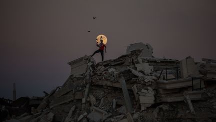 Un jeune Palestinien jongle, perché sur les ruines d'un bâtiment détruit par les bombardements de l'armée israélienne, tandis que la "super Lune" éclaire le camp de réfugiés d'Al-Bureij, le 15 novembre 2024, dans la bande de Gaza.